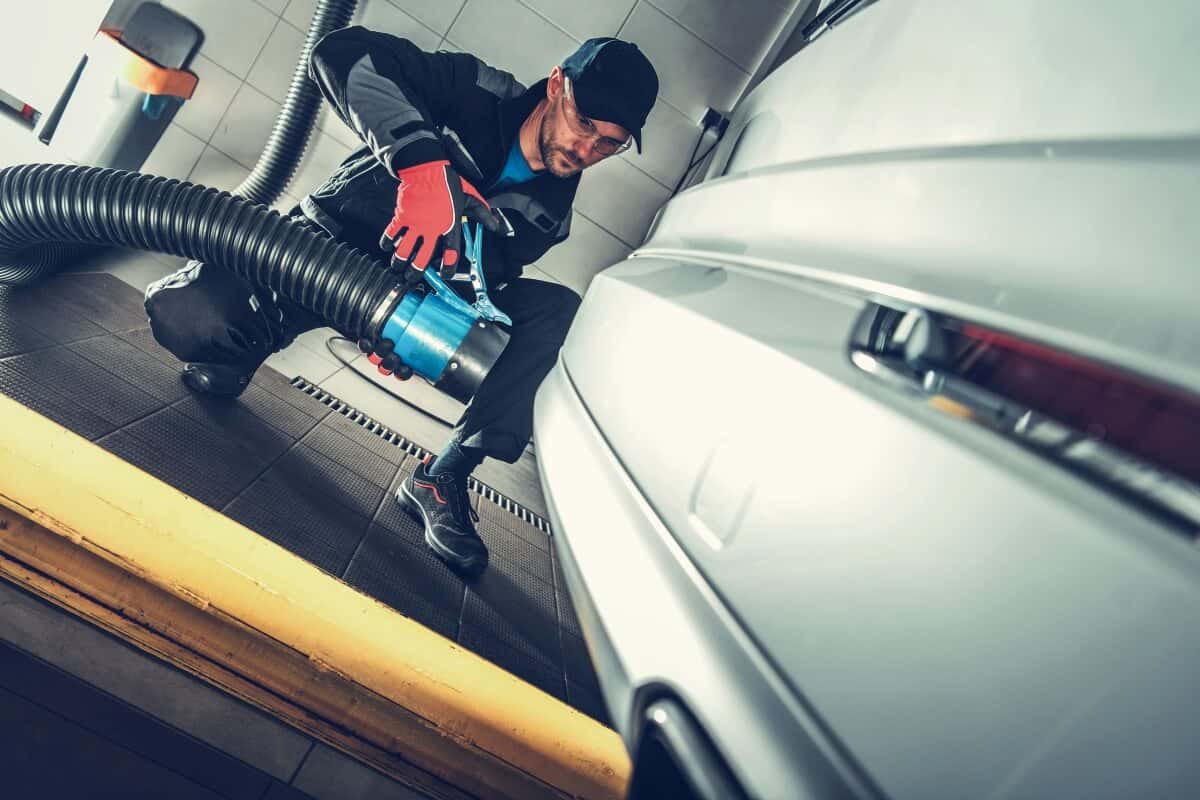 Mechanik wykonuje regenerację katalizatora SCR przy białym samochodzie.