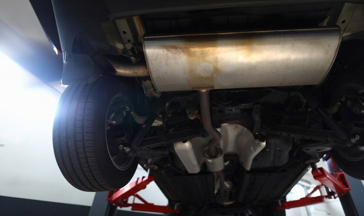 Widok spod samochodu na podniesionym podnośniku podczas czyszczenia filtra DPF.