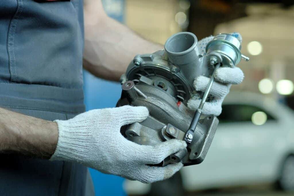 Mechanik trzyma turbosprężarkę, co symbolizuje proces regeneracji turbosprężarki.