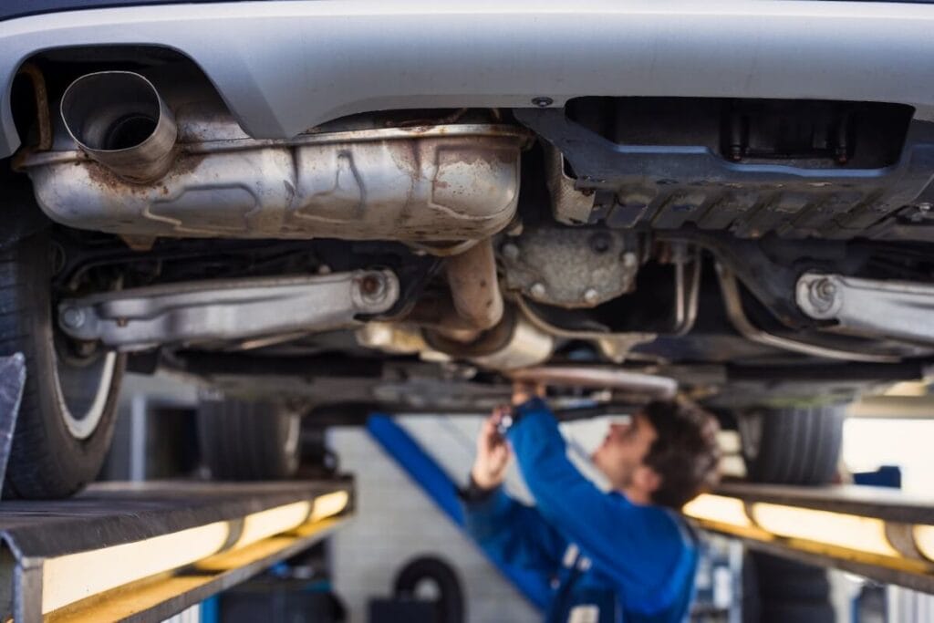 Mechanik pracuje pod podniesionym samochodem, wykonując czyszczenie filtra DPF.