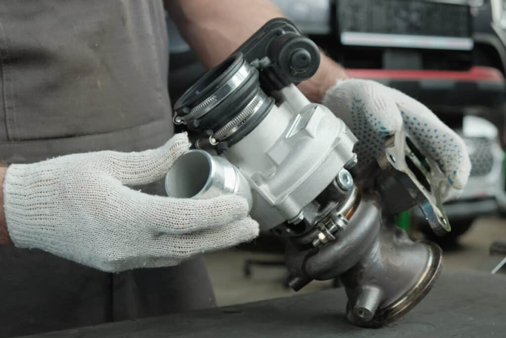 Technik w rękawiczkach przeprowadza regenerację turbosprężarki, trzymając jej elementy na blacie warsztatowym.