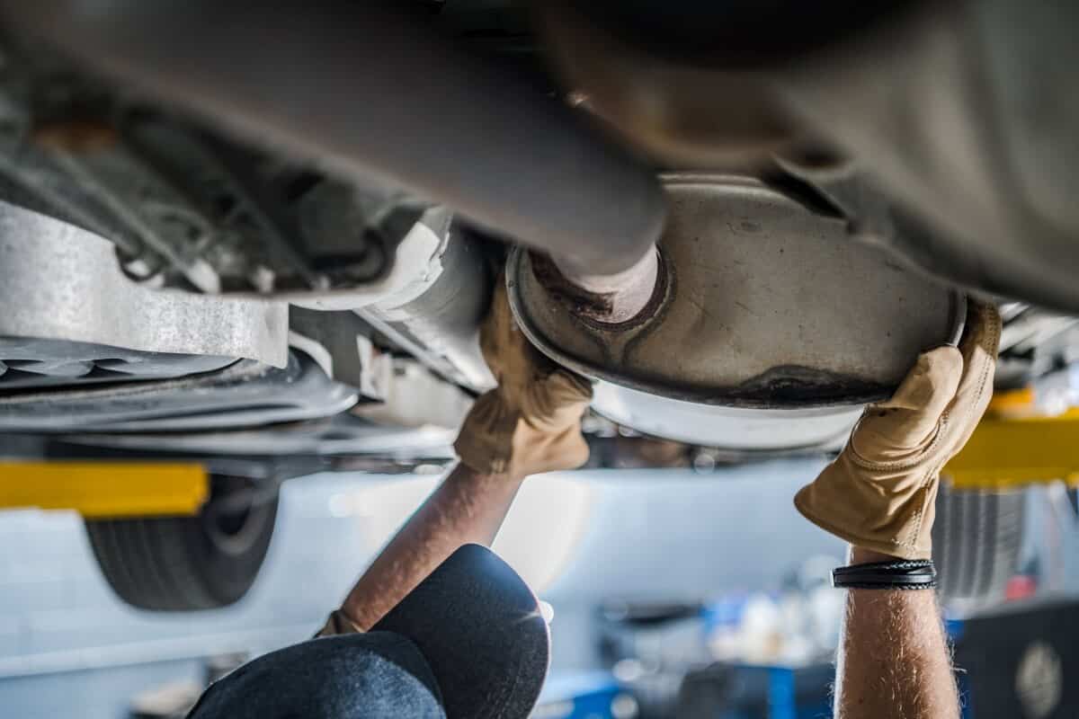 Mechanik pod uniesionym samochodem trzyma element wydechu podczas czyszczenia filtra DPF