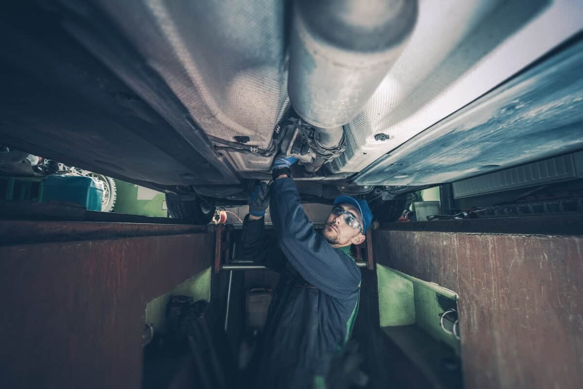 Mechanik w kanale serwisowym sprawdza układ wydechowy auta, rozważając regenerację katalizatora SCR