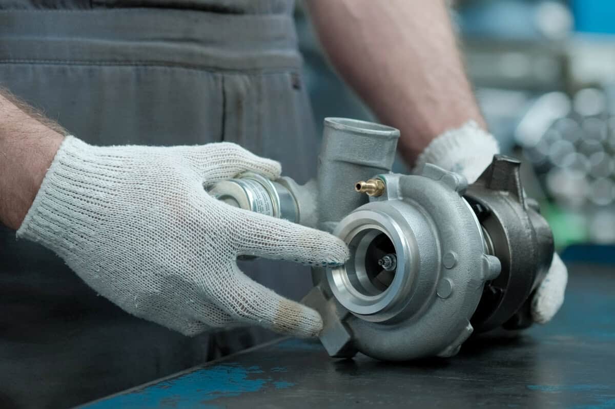 Mechanik w rękawicach sprawdza turbosprężarkę po regeneracji turbosprężarki przy stole warsztatowym